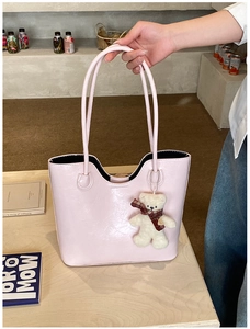Detail of light pink glossy leather tote bag with wavy edge and cute teddy bear charm