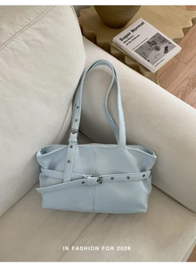 Detail of light blue tote bag with buckle straps and silver eyelets on a sofa