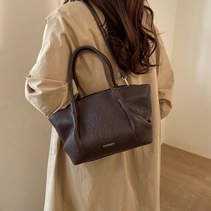 Détail du sac cabas marron foncé à texture vintage et logo argenté sur un trench-coat beige
