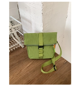 Détail du sac bandoulière à carreaux verts avec boucle et tirette de fermeture orange