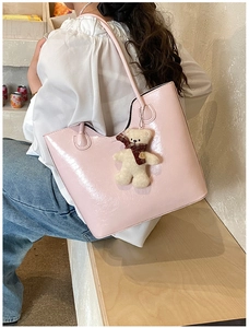 Detail of pink glossy faux leather tote bag featuring a cute plush bear charm with scarf