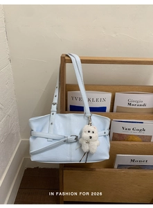 Detail of light blue tote bag with metallic buckle and white plush puppy charm