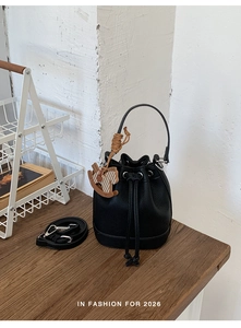 Detail of black leather bucket bag with drawstring closure and brown horse charm on a wooden table