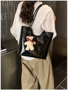 Detail shot of large black patent leather tote bag with cute beige bear charm on a model