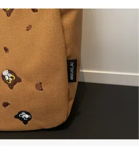 Detail of brown canvas tote bag featuring colorful cat embroidery and brand woven label