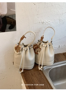 Detailed view of beige drawstring bucket bag in litchi grain leather with horse charm