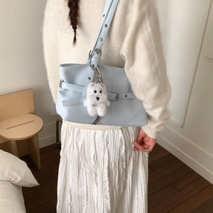 Detail of light blue tote bag with strap buckle and plush puppy charm on model shoulder