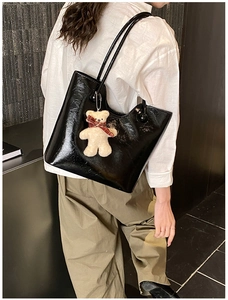 Detail of glossy black tote bag with shoulder straps and cute plush bear accessory