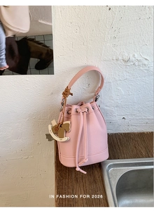 Close-up of pink lychee grain leather bucket bag with drawstring and wooden horse charm