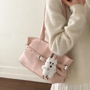 Detail view of light pink leather tote bag with silver buckle and plush dog charm on shoulder
