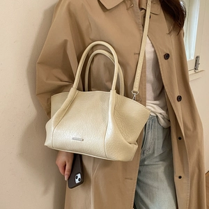 Détail d'un sac cabas crème avec texture froissée, porté par un mannequin en manteau beige