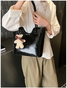 Detail of glossy black leather tote bag featuring a cute plush bear charm with scarf