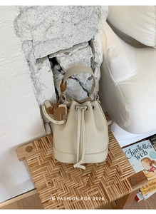 Detail of off-white lychee leather bucket bag with drawstring and wooden horse charm