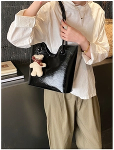 Detail of black glossy tote bag with vintage texture and cute plush bear charm accessory