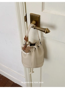 Detail of cream drawstring bucket bag with grain leather texture and horse charm