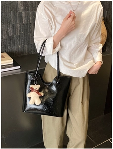 Close-up of black glossy tote bag featuring a cute beige plush bear pendant accessory