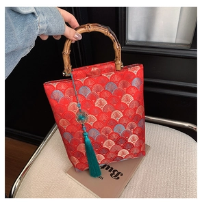 Close-up of red embroidered brocade bag with bamboo handle and green silk tassel detail