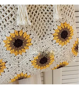 Close-up of handmade woven tote bag with yellow sunflower pattern and beige tassel trim