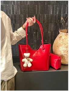 Detail of red glossy tote bag featuring a white teddy bear charm and matching pouch