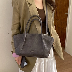 Détail d'un sac cabas en cuir texturé marron foncé porté avec un blazer kaki élégant