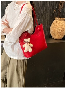 Detail of red faux leather tote bag with plush bear charm and grid bow accessory