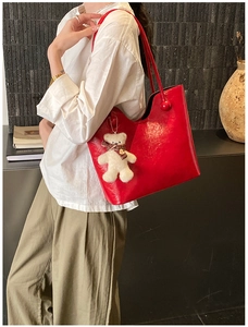 Detail of red faux leather tote bag with plush bear charm and spherical handle accents