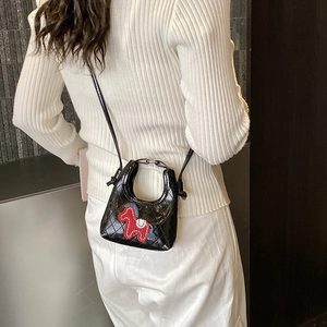 Detail view of black quilted mini dumpling bag with red horse patch on white knitwear