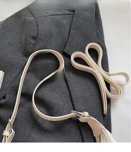 Dettaglio della tracolla regolabile in pelle beige con fibbie in metallo argento su giacca