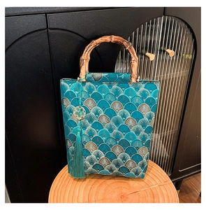 Close-up of blue embroidery handbag featuring traditional bamboo handles and a silk tassel