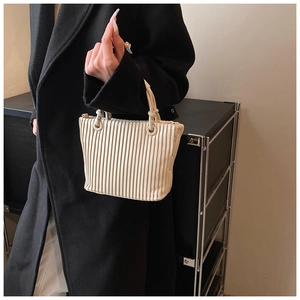 Detailed view of cream pleated handbag with knotted handle detail on black coat background