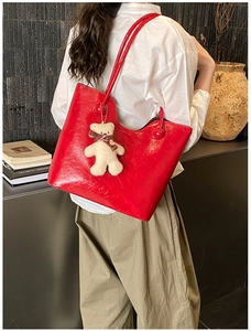 Detail of red glossy leather tote bag with cute plush bear charm in a modern lifestyle setting
