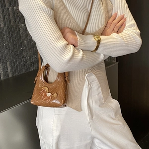 Close-up of a brown quilted mini bag with a cute horse charm worn on a knit outfit