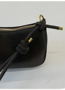 Detail of dark leather bag showing knot strap design and golden metallic zipper