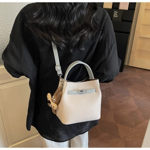 Detail view of cream bucket bag featuring contrast light blue handle and cute bear charm