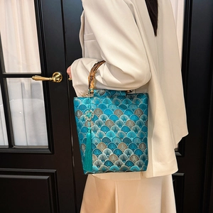 Detail of teal jacquard tote with mountain pattern, bamboo handle, and silk tassel charm