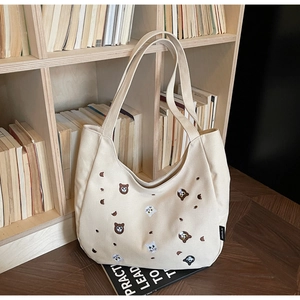 Detail of cream canvas tote bag featuring cute animal embroidery and branded side label