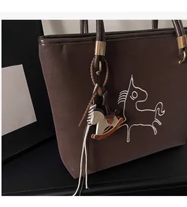 Detail of dark brown leather tote featuring white horse embroidery and a colorful horse charm