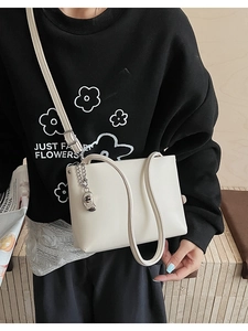 Close-up of cream PU leather handbag with silver chain and bean-shaped metal pendant
