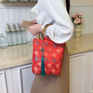 Close-up of red embroidery handbag featuring bamboo handle and green silk tassel charm