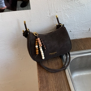 Detail view of brown suede dumpling bag with fashion logo and wooden bead tassel decor