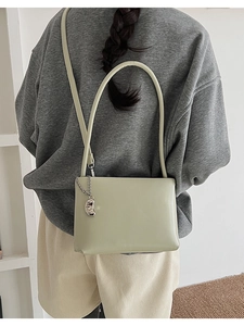 Detail of light green rectangular shoulder bag featuring silver chain and metal charm