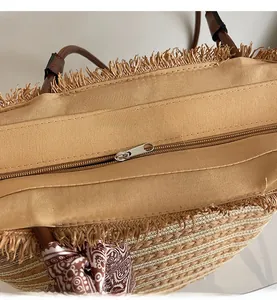 Detail of straw tote bag showing smooth metal zipper closure and leather handle with scarf
