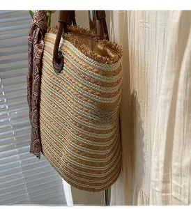 Detail of straw tote bag with horizontal stripes, brown leather handles and decorative scarf