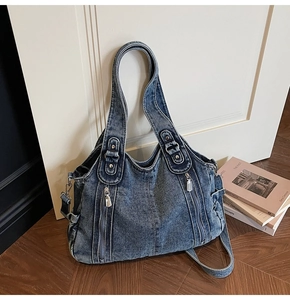 Detail shot of blue denim tote bag with silver zippers and side pockets on wooden floor