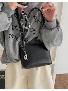 Detail of black leather crossbody bag featuring a silver moon charm and metal chain strap