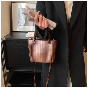 Detail view of caramel brown pleated bucket bag with cylinder handle and slim shoulder strap
