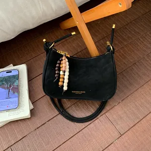 Detail of black matte leather shoulder bag with wooden bead charm and golden zipper