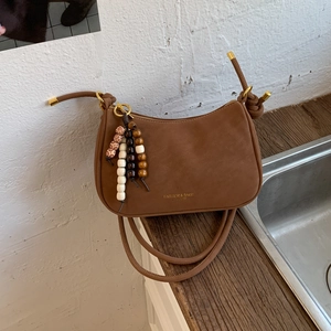 Detail of a brown suede half-moon bag with wooden bead tassel and fashion gold logo