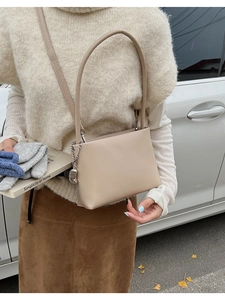 Outdoor shot of a beige PU leather crossbody bag with a metallic chain charm