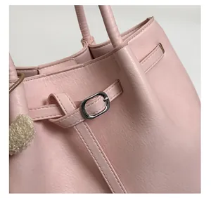 Détail du sac seau en cuir rose avec boucle argentée et accessoire pompon en peluche beige